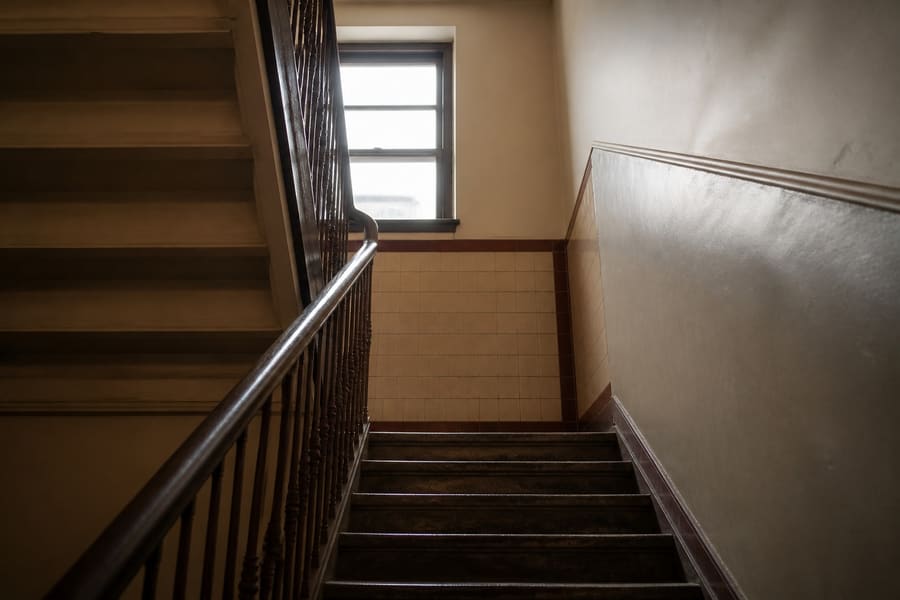 A narrow tenement stairwell with worn treads leading up past a landing