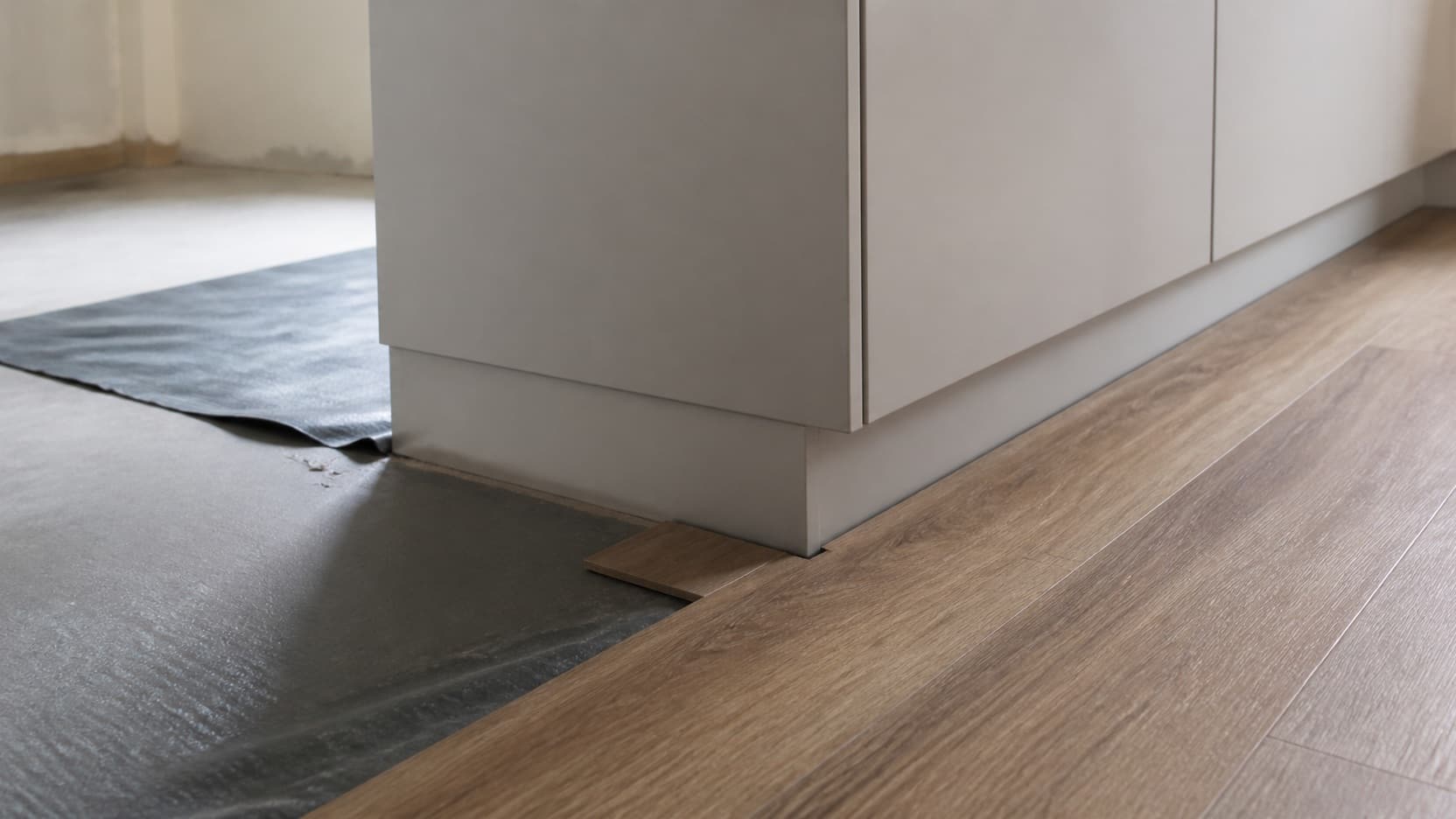 Luxury vinyl plank being laid in a kitchen with cabinetry and a sink run visible behind